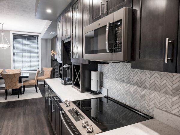 A modern kitchen with dark cabinets, a microwave, stovetop, and a light dining area with seating for four.