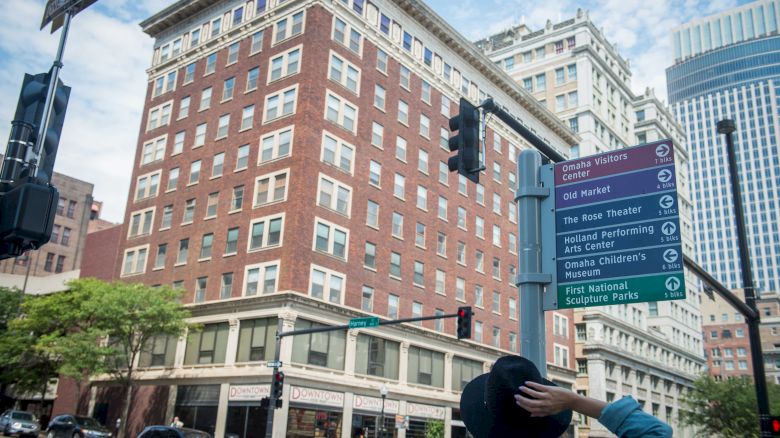 A person looks at a street sign displaying local attractions in an urban area with tall buildings and clear skies in the background.