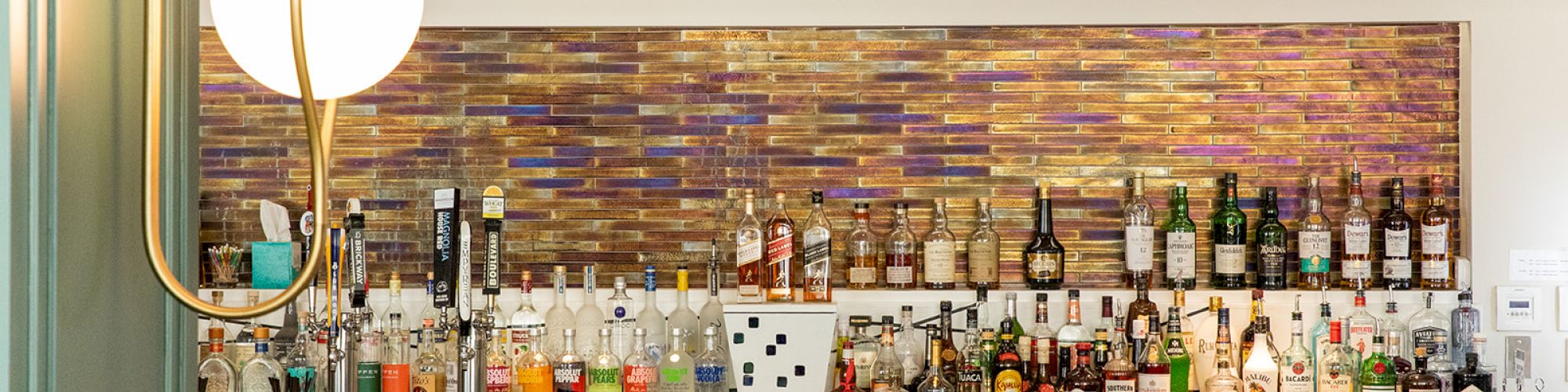 The image shows a stylish bar with a variety of liquor bottles, elegant seating, and decorative wall paneling.