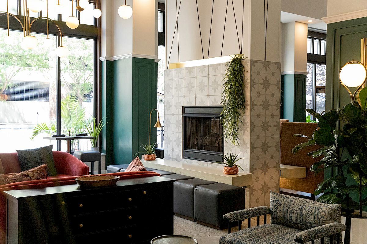 A cozy living space featuring a fireplace, modern furniture, plants, and ample natural light from large windows and elegant lighting fixtures.