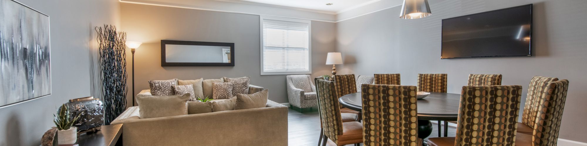 A modern living-dining area with a sofa, dining table, chairs, TV, and decor items, featuring gray walls and wooden flooring.