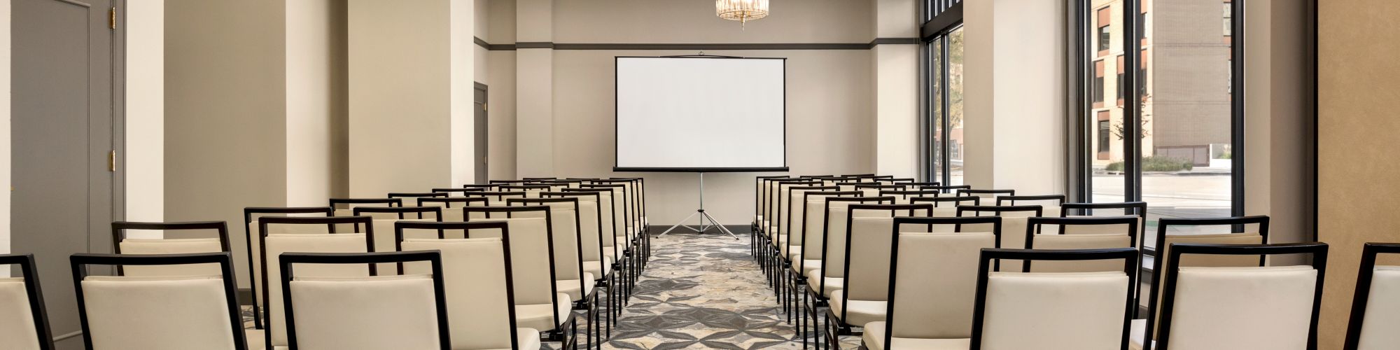 The image shows an empty conference room with rows of chairs facing a screen, and decorative lighting above.