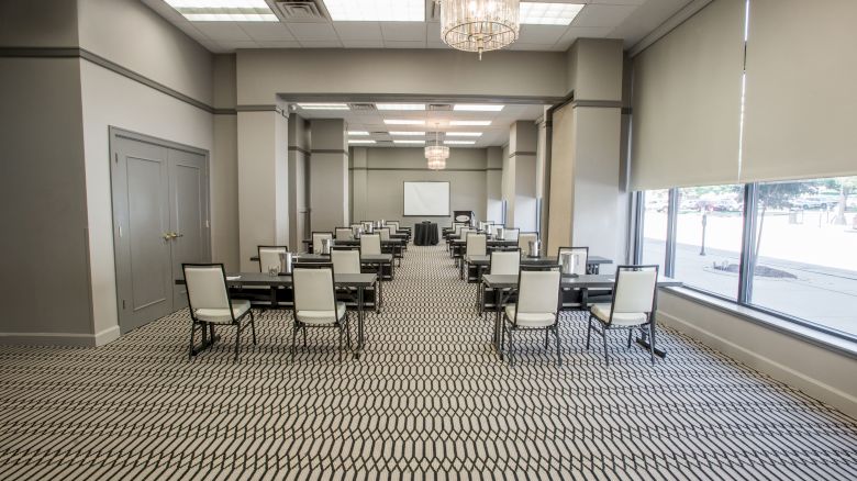 The image shows a modern conference room with rows of chairs and tables facing a projector screen, under elegant chandeliers.