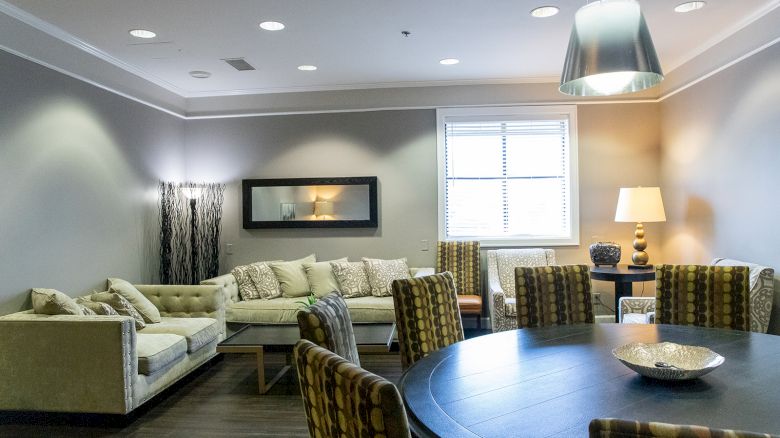 A modern living room with a sectional sofa, patterned chairs around a circular table, pendant light, and table lamps.