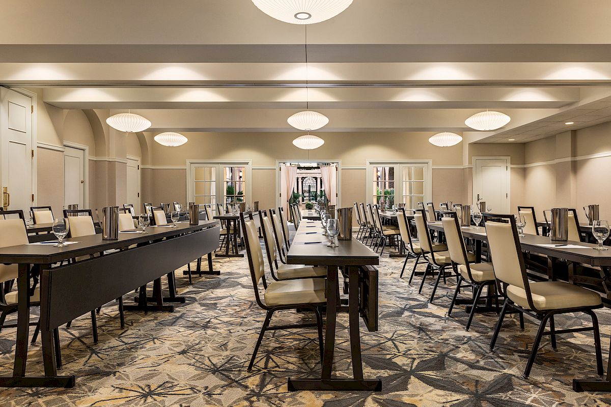 The image shows an empty conference room with neatly arranged tables and chairs, illuminated by ceiling lights, featuring a patterned carpet.