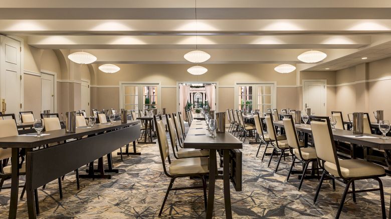 The image shows an empty conference room with neatly arranged tables and chairs, illuminated by ceiling lights, featuring a patterned carpet.