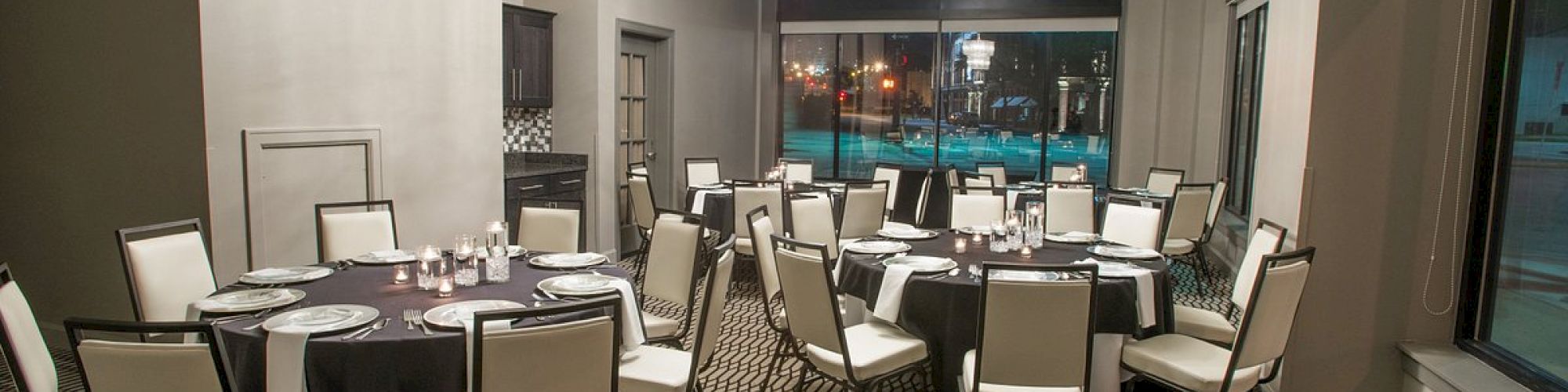 A modern dining room with round tables and white chairs, set with tableware, under elegant lighting.