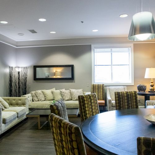 A modern living-dining room with sofas, a round table, patterned chairs, and soft lighting.