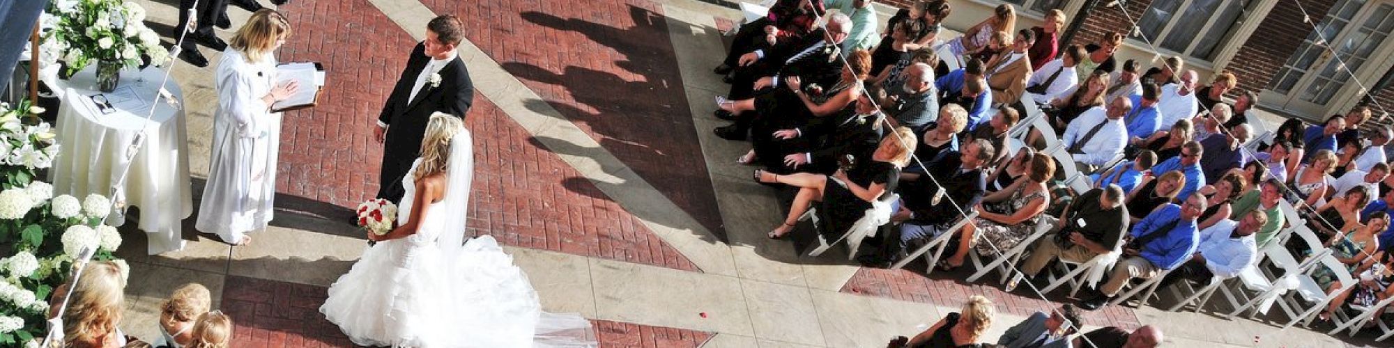 A wedding ceremony with a bride and groom, bridesmaids, groomsmen, and seated guests in an outdoor setting.