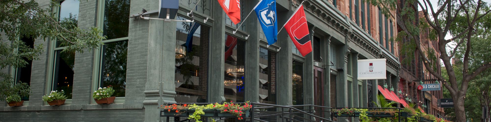 A multi-story building with flags, including a Marine Corps flag, and a wheelchair ramp on a city street with trees.