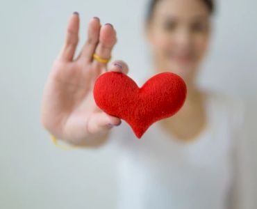 A person holding a red heart-shaped object in focus while the background is blurred, conveying a feeling of warmth and affection.