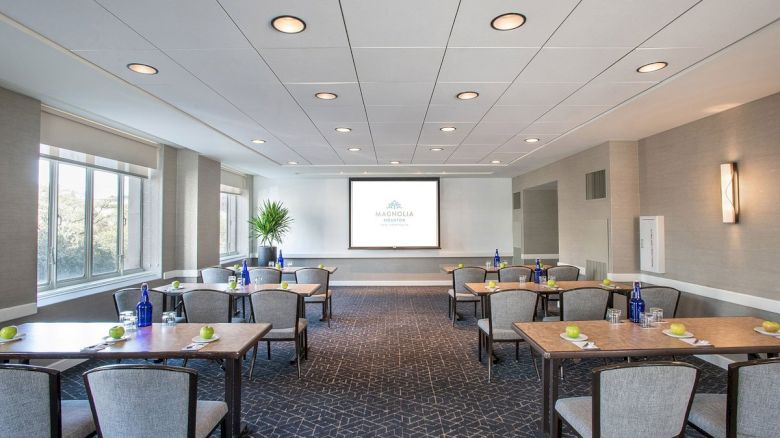 A modern conference room with tables, chairs, water bottles, and notepads arranged, facing a screen displaying a logo or presentation.