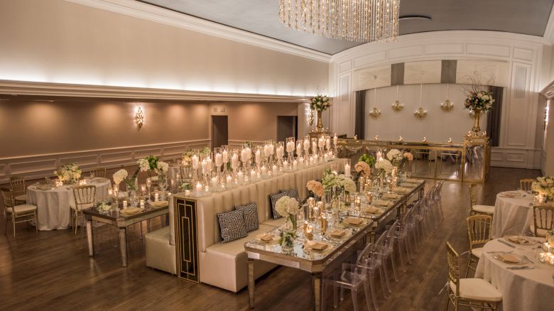 An elegant banquet hall with candlelit tables, floral arrangements, and gold accents, set for a formal event or reception.