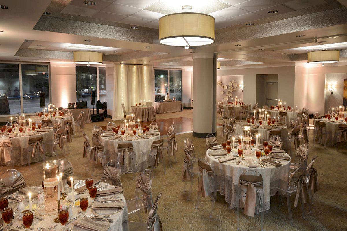 The image shows an elegantly decorated banquet hall with round tables, chairs with covers, and candles, set for a formal event or reception.
