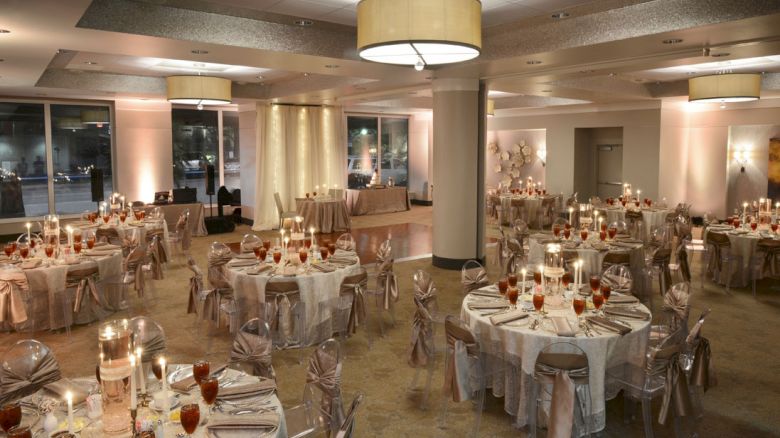 The image shows an elegantly decorated banquet hall with round tables, chairs with covers, and candles, set for a formal event or reception.