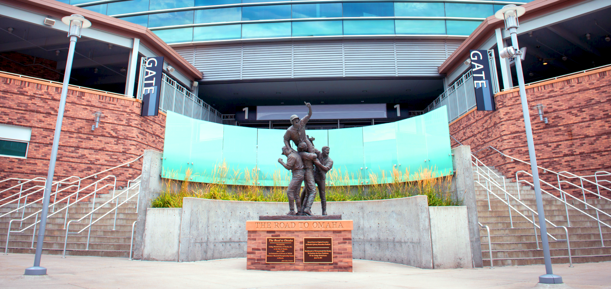 A bronze statue of three figures stands in front of a building entrance with stairs, signs for gates, and glass panels.