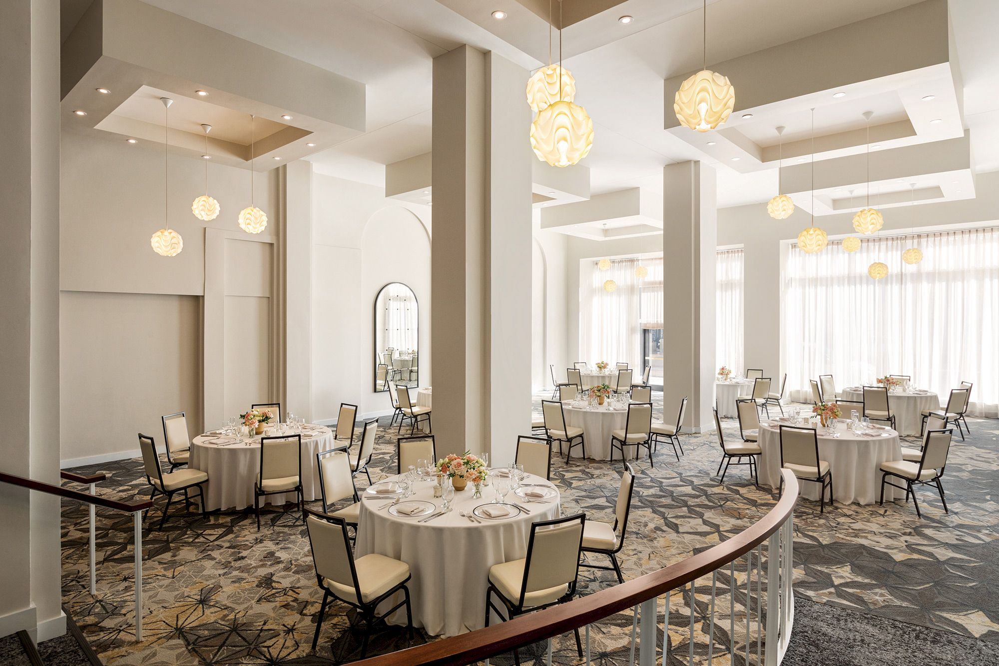 The image shows an elegant banquet hall with round tables, chairs, floral centerpieces, and pendant lights, featuring large windows and columns.