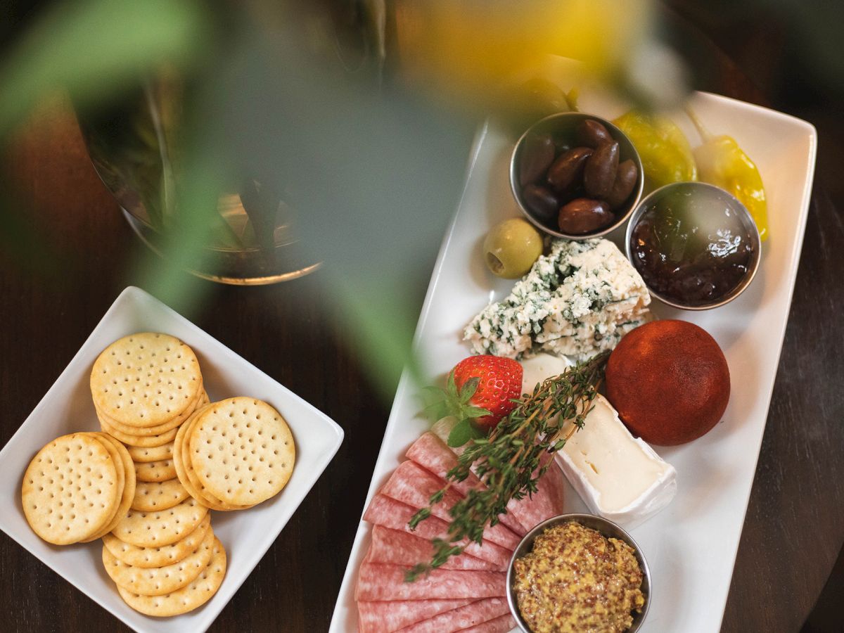 A cheese and charcuterie platter with crackers, olives, salami, cheese, mustard, and a tomato on plates.