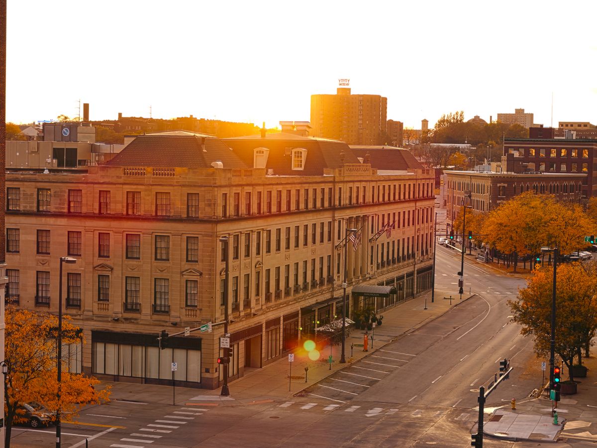 A quiet city street with historic buildings, surrounded by autumn trees, under a warm sunrise glow.