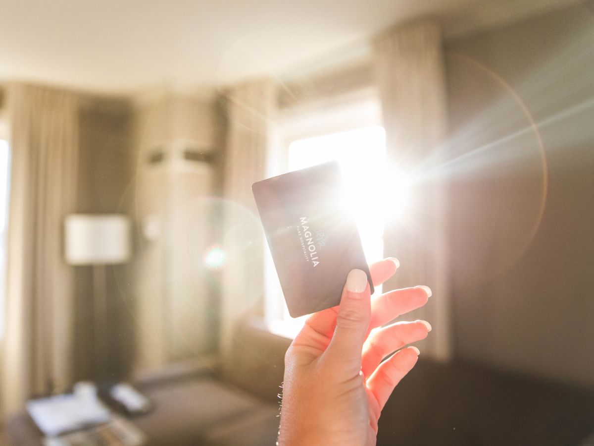 A hand holding a card in a sunlit room, with sunlight creating a bright flare, and furniture visible in the background.