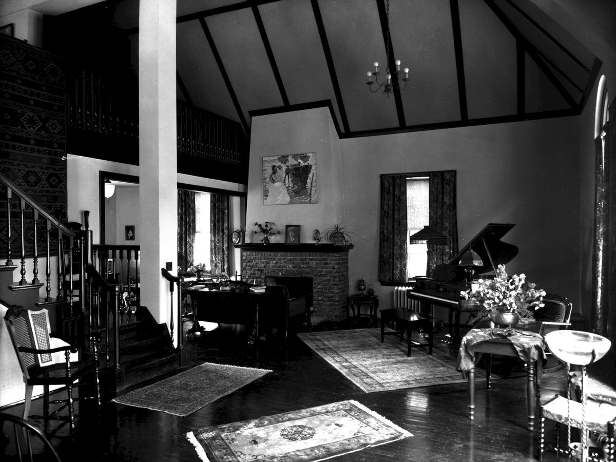 A cozy living room with a high ceiling, featuring a fireplace, a grand piano, chairs, rugs, and a table with flowers, creating a warm ambiance.