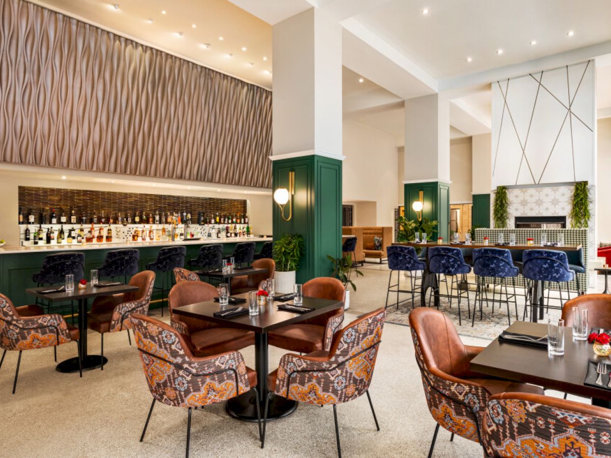 This image shows a modern restaurant with patterned chairs, a bar with bottles, and a stylish, open interior design.