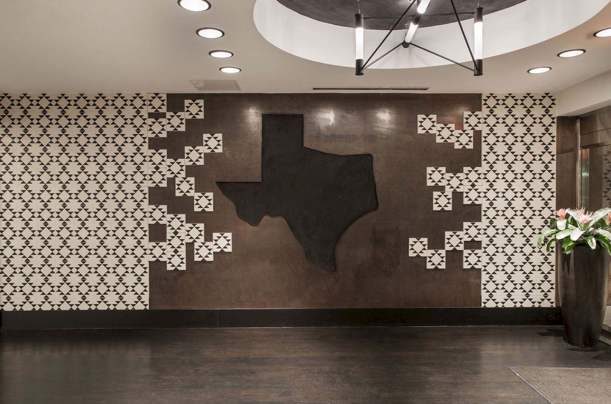 The image shows a wall with a large map of Texas surrounded by black and white patterned tiles in a modern interior setting.