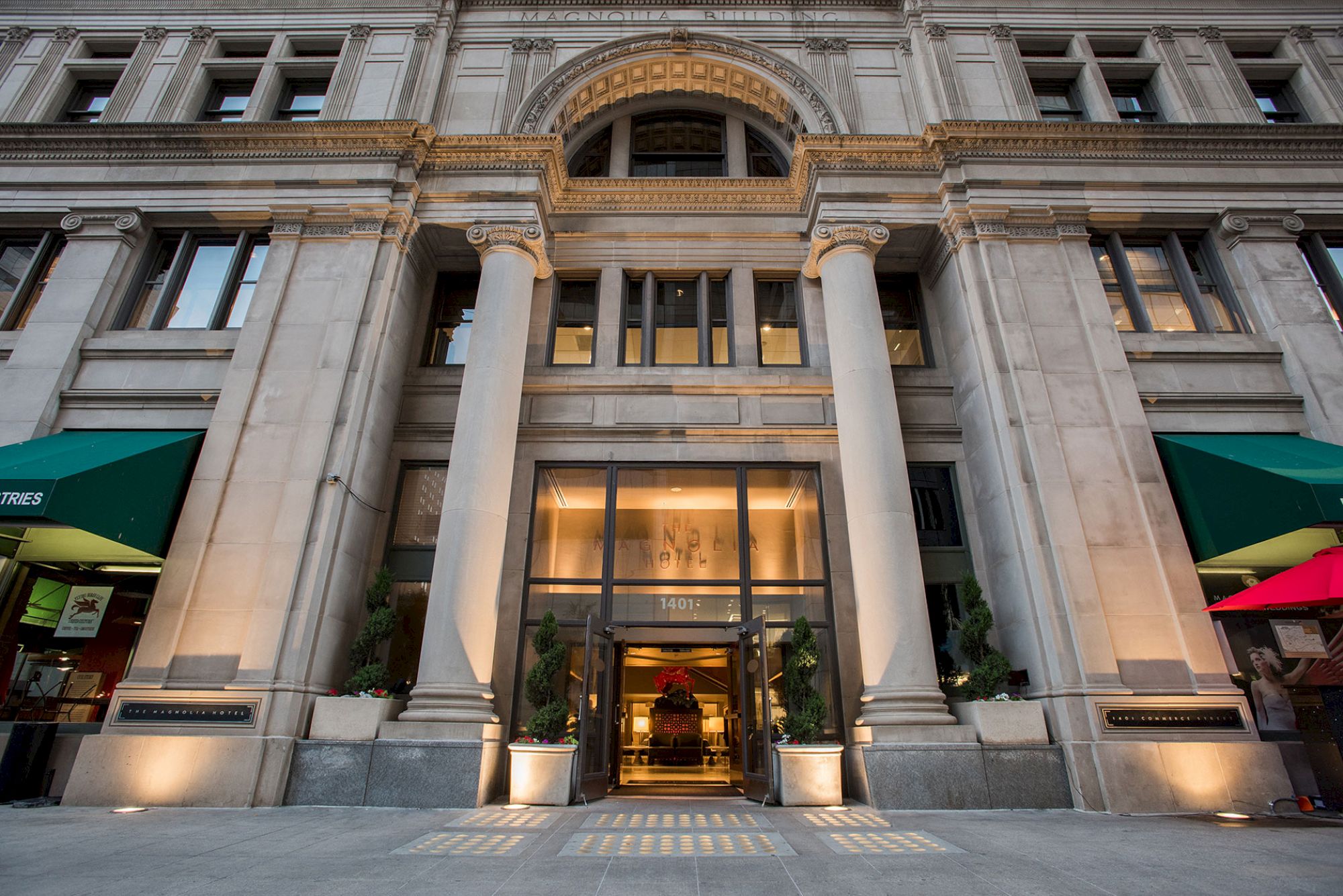 The image shows the entrance of a grand building with tall columns and an arched facade, illuminated by exterior lights.