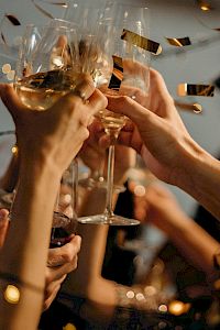 A group of people are raising glasses in a celebratory toast, surrounded by festive lights and confetti.