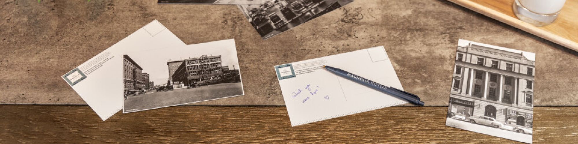 A desk with vintage postcards, a pen, cookies on a tray, a glass of milk, and a potted plant.