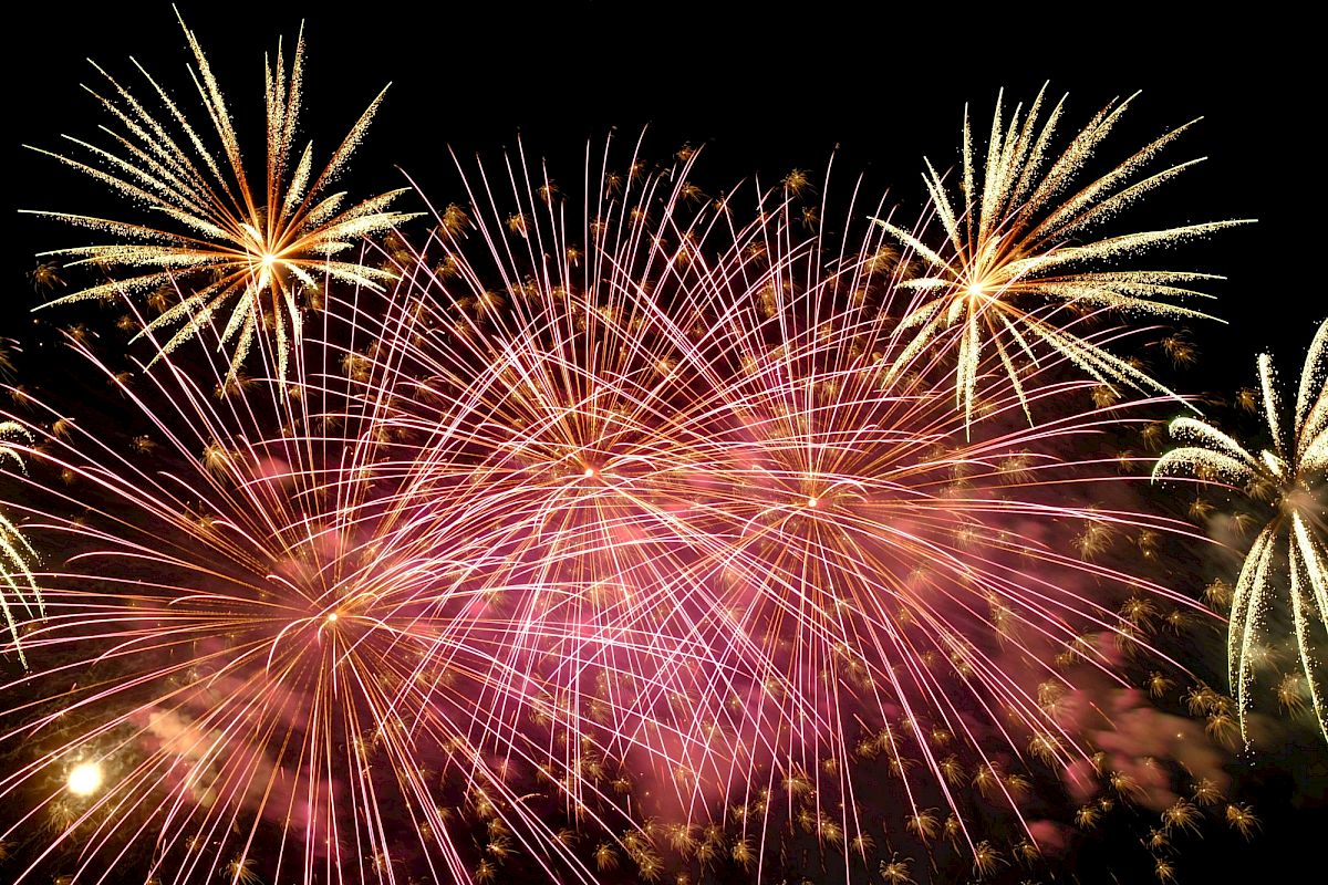 A vibrant fireworks display with bursts of pink and gold against a dark night sky, creating a festive and celebratory atmosphere.